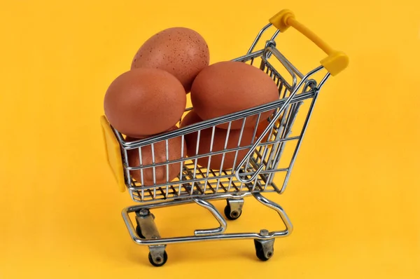 Supermarket trolley full of chicken eggs close-up on a yellow background