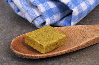 Bouillon cube in a wooden spoon with a kitchen towel close-up on a gray background