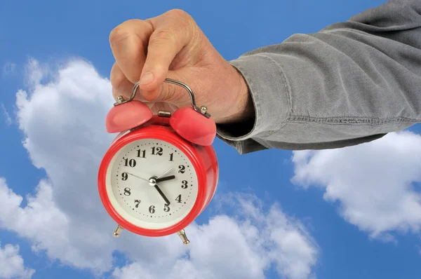 Alarm clock held in hand on sky background with clouds