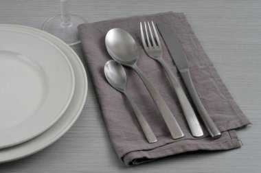 Cutlery on a napkin with plates and a glass close-up