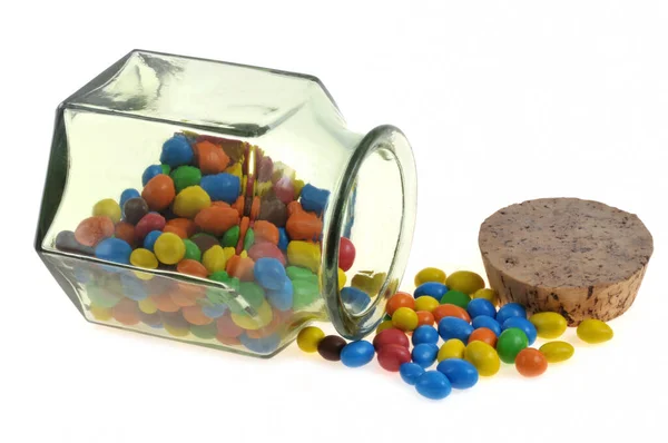stock image Jar of chocolate covered peanuts of different colors spilled on white background 