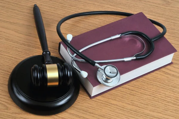 Medical error concept with a stethoscope lying on a book and a judge gavel on a wooden background