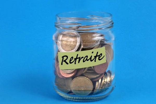 Glass jar filled with money with a label that says retirement in french closeup on blue bakground