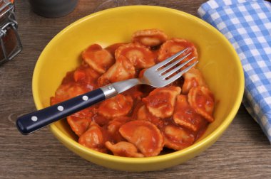 Domates soslu Ravioli, yakın plan çatallı sarı bir tabakta servis edilir.