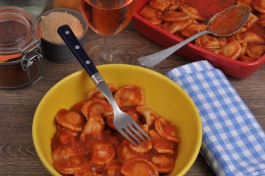 Sarı bir tabakta servis edilen domates soslu Ravioli ve bir bardak şarap ve bir ramekin parmesan peyniri.