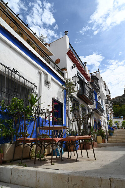 Houses lined with plants in an old quarter of Alicante with a table and chairs in the foreground