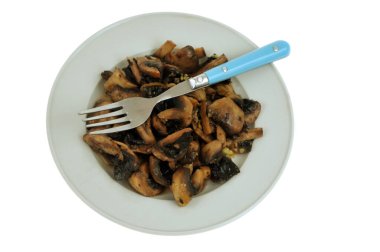 Beyaz arka planda çatalla yakın plan sarımsakla pişirilmiş mantarlar.