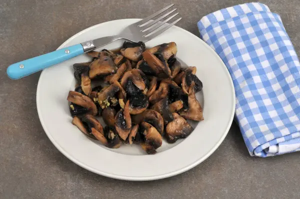 Tabakta sarımsakla pişirilmiş mantarlar ve gri arka planda bir çatal yakın plan. 