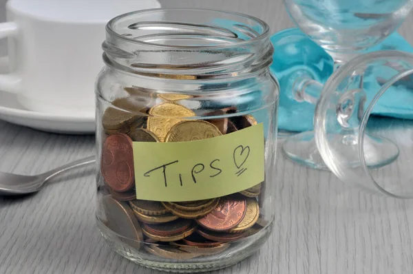 Tip jar filled with coins placed on a table with tableware in the background
