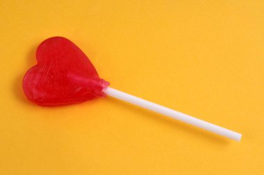 Kalp şeklinde çilek lolipopu sarı arka planda.