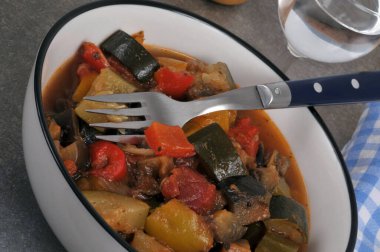 Bir tabak ev yapımı ratatouille, çatal ve bir bardak su.
