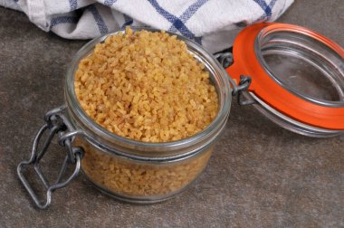 Kavanoz dolusu açık ham bulgur buğdayı gri arkaplanı kapatır 
