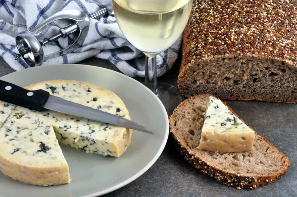 Fourme d\'Ambert on a plate with a knife and seeded bread and a glass of wine