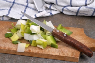 Çiğ pırasa, tahta kesme tahtasının üzerinde bıçakla parçalara ayrılmış.