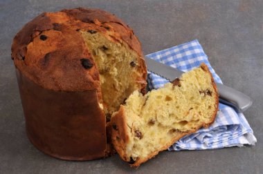 Gri arka planda bıçak ve peçeteyle dilimlenmiş panettone.