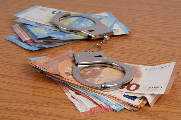 Financial crime concept with handcuffs on wads of euro banknotes closeup