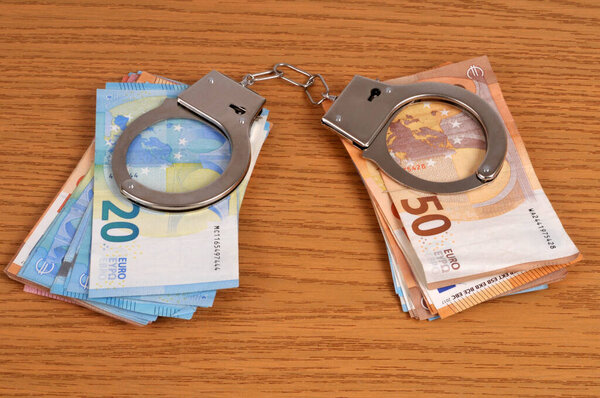 Financial crime concept with handcuffs on wads of euro banknotes