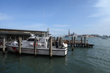 İskeleye demirlemiş bir sahil güvenlik botu ve arka planda da San Giorgio Maggiore Bazilikası var.