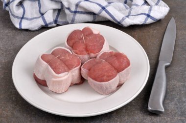 Three raw veal paupiettes on a plate with a knife close-u clipart