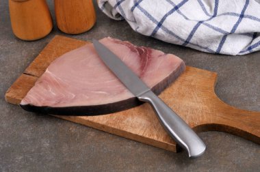 Kesme tahtasının üzerinde bıçakla çiğ kılıç balığı dilimi.