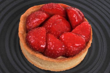 Çilekli tart, siyah bir tabakta yakın plan.
