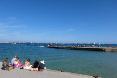 Larmor-Plage 'daki Toulhars sahilinde oturan genç turistler.