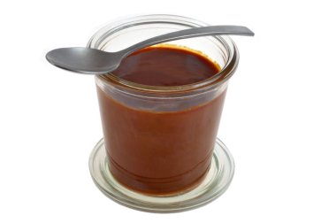 Ev yapımı tuzlu karamelli ramekin kaşıkla yakın plan beyaz arka planda izole edilmiş.