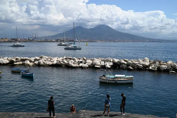 Napoli 'deki Molo Luise marinasında, arkasında Vesuvius volkanı olan turistler.