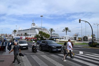 Cadiz limanındaki yaya geçidinde arka planda bir yolcu gemisi olan insanlar var.