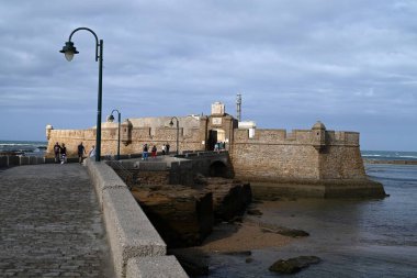 Deniz duvarında yürüyen turistler Castillo de San Sebastian 'a gidiyor.