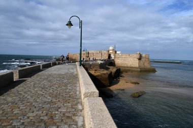 Deniz duvarında yürüyen turistler Castillo de San Sebastian 'a gidiyor.