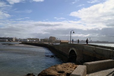 Deniz duvarında yürüyen turistler Castillo de San Sebastian ile Cadiz şehrini birbirine bağlıyorlar.