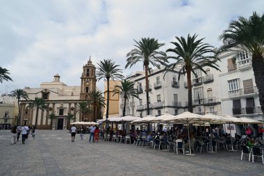 Cadiz 'deki Katedral Meydanı' nın arka planında turistlerle ve Havari Santiago 'nun kilisesiyle dolu kafe terasları.