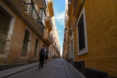 Cadiz şehrinde dar bir cadde boyunca yürüyen turistler tipik Endülüs mimarisine sahip binalarla dolu.