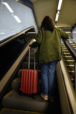 Madrid metrosunun yürüyen merdiveninde bavullu bir kadın.