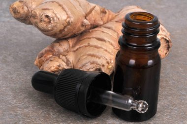 Bottle of ginger essential oil with its pipette and fresh ginger close-up on a gray background clipart