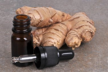 Bottle of ginger essential oil with its pipette and fresh ginger closeup isolated on a gray background clipart