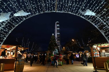 Vannes şehrindeki Noel pazarına girişte arka planda bir dönme dolap ve insanlar geziniyor.