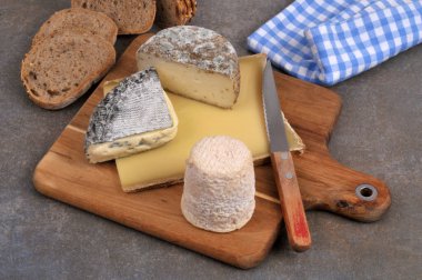 Tahta kesme tahtasındaki Fransız peynirlerinin çeşitli çeşitleri. Gri arka planda bir bıçak ve dilimlenmiş ekmek ile.