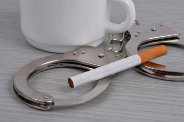 Concept of penalization of smoking a cigarette with handcuffs lying on a table next to a cup of coffee clipart