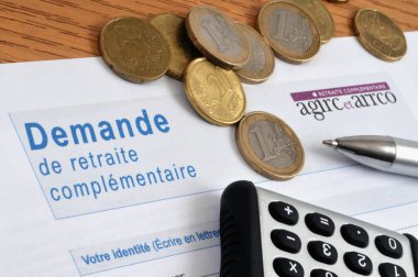 Agirc-Arrco tamamlayıcı emeklilik başvuru formu ile bir hesap makinesi ve avro sikkeleri