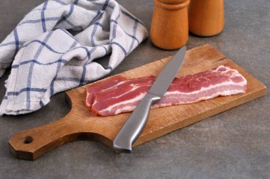 Kesme tahtasının üzerinde füme pastırma dilimleri ve gri arka planda yakın plan bir bıçak.