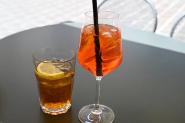 Bir bardak spritz ve masada bir bardak buzlu çay.