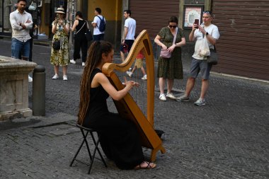 Yukarı kasabadaki Bergamo 'da turistlerin önünde arp çalan genç bir kadın.