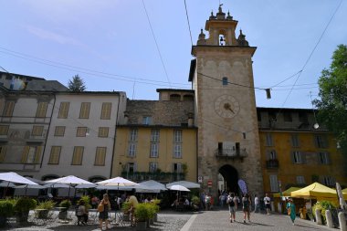 Bergamo 'nun üst kasabasındaki Piazza della Cittadella' da restoran terasları ve turistleri olan saat kulesi.