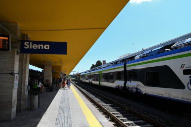 Güneşli bir günde tren ve yolcularla Siena tren istasyonu platformu
