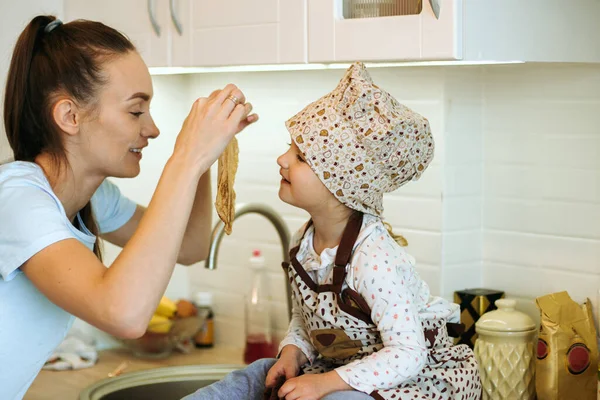可愛いお母さんと一緒に可愛い家庭料理の女の子が白いキッチンでパンケーキを作ってる ハッピーファミリーキッチンタイム — ストック写真