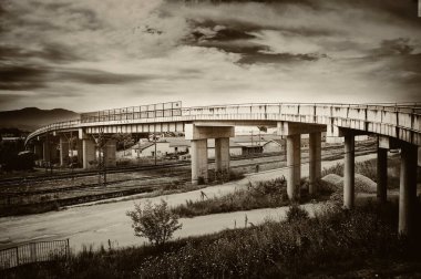 Beton sütunlar ve asfalttan inşa edilmiş bir üst geçit, yüksek hızlı trenlerin geçtiği rayların üzerinden geçer..