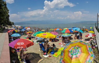 Dojran, Makedonya - 19 Temmuz 2016 Dojran Gölü 'nün sularında çadırları, güneşlikleri ve serinleyen insanlarla dolu bir plajın panoramik fotoğrafı.