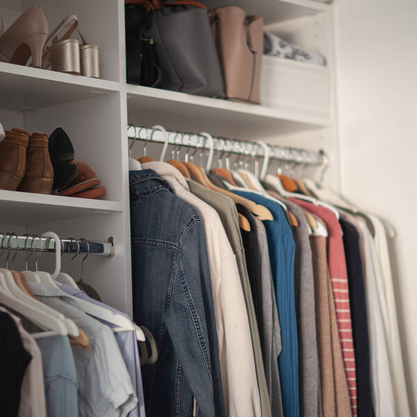 белый шкаф крупным планом, одежда висит на вешалках и обуви, квадратный формат